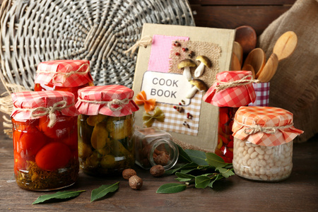 罐腌制的蔬菜和豆类 香料 食谱和厨房用具的木制背景上的书