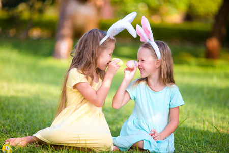 两个可爱的小姐妹玩蛋头戴在复活节的兔子耳朵