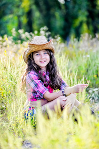 小女孩坐在戴着一顶牛仔帽的字段