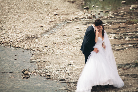 优雅温柔时尚新郎和新娘用石头河附近。婚礼热恋中的情侣