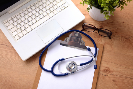 附近一台笔记本电脑上木桌前，在白色的医用听诊器