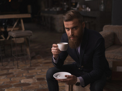 有魅力的留胡子的商人正在享受热咖啡