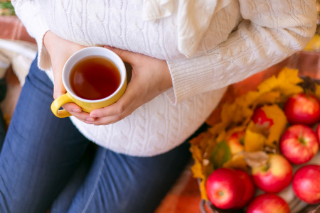 怀孕的妇女抱着一杯茶，坐在格子中