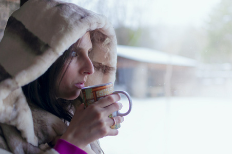 在窗户里喝茶的女人看着寒冷的冬日, 意思是透过窗户