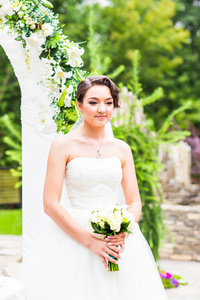 美丽的新娘女孩穿着婚纱时用束鲜花，户外肖像