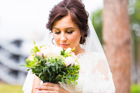 美丽的新娘女孩穿着婚纱时用束鲜花，户外肖像