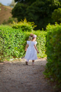 穿着白色连衣裙的小女孩在公园里行走在一条小径