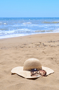 太阳镜和躺在打击海的海滩上的沙子上的那顶草帽