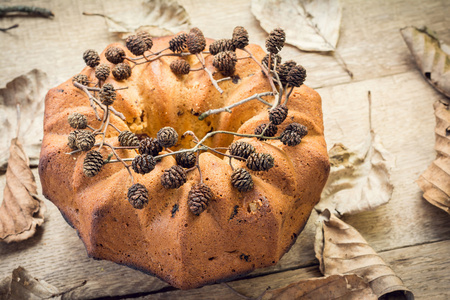 甜蜜的蛋糕装饰桤木的球果,干燥叶上木制背景照片