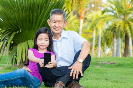 亚洲的祖父和孙子正在公园与智能手机自拍照