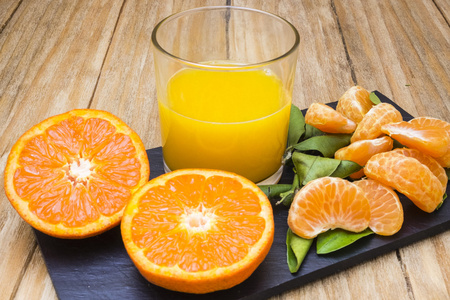 几个成熟的柑橘和一杯果汁在黑板上木制的桌子上