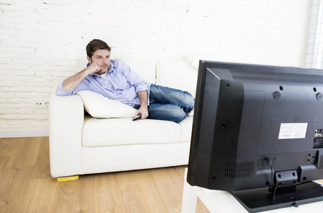 年轻快乐的人，躺在家里看轻松享受电视的客厅沙发上看电视