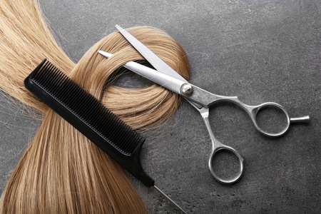 发型师的剪刀梳子与钢绞线的金发在灰色的背景上照片