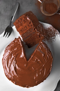 巧克力蛋糕上切的一块板和叉可可灰色背景，特写