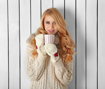 热的饮料杯的年轻美丽的金发女人，在她针织暖和的衣服，冬天肖像