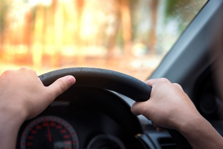 s hands of a driver on steering wheel of a minivan car on high w