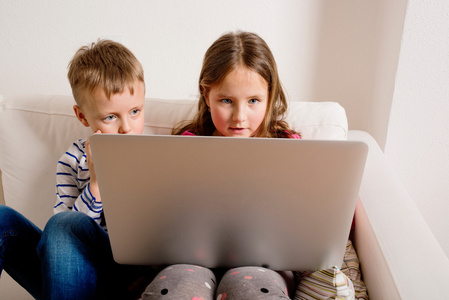 孩子们在家里坐在沙发上，玩笔记本电脑