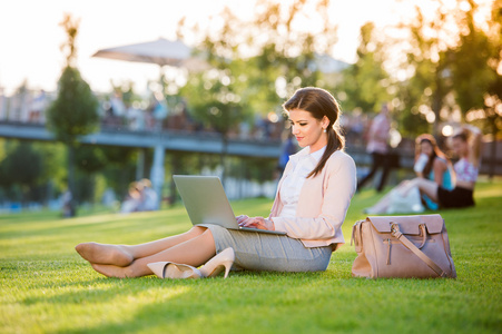 女商人坐在公园里用笔记本电脑工作，阳光明媚的夏天