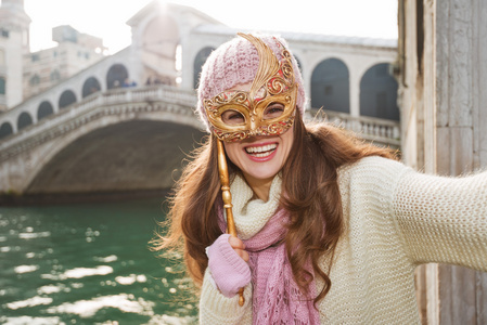 带着威尼斯面具的微笑女人在里尔托桥附近自拍