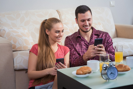 可爱的年轻夫妇在手机上吃早餐照片