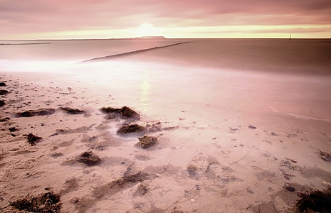 在波浪波罗的海上的木制防波堤。与第一个炎热的太阳光线的粉红色地平线