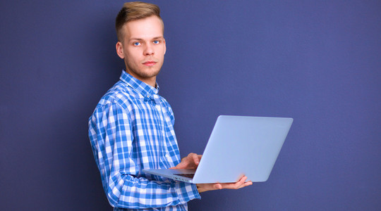 自信的年轻人用笔记本电脑站立在灰色背景的肖像