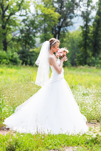 美丽的新娘与户外中绿色公园的婚礼花束