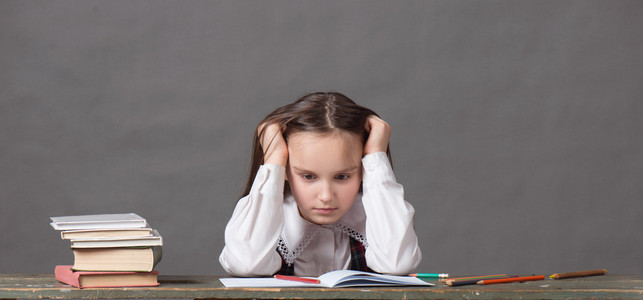 穿着校服的女孩坐在桌前书，灰色的背景下，看起来像粉笔板