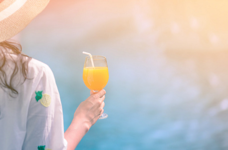美丽的女人，戴着帽子的后视举行橙汁玻璃池畔在夏天