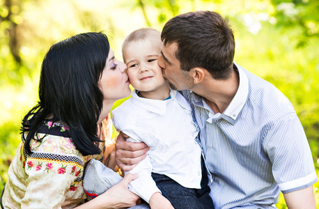 幸福的母亲和父亲亲吻他的小儿子在公园