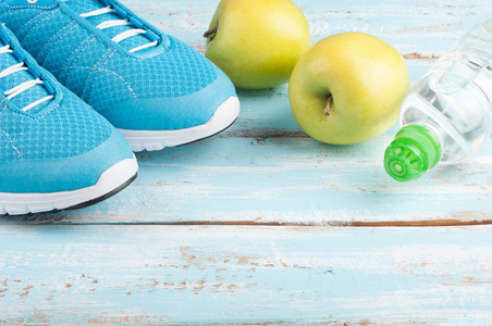 运动鞋，苹果，瓶水在蓝色木背景