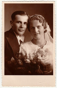 新婚夫妇的婚礼花束的老式照片。新娘穿婚礼面纱头饰。新郎穿时髦的衣服，白色领结。黑色与白色的古董室画像