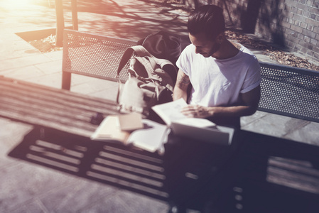 穿着白色T恤坐在城市公园看书的年轻人