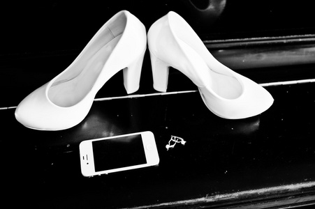 在钢琴配有电话和耳环新娘的白色婚礼鞋子