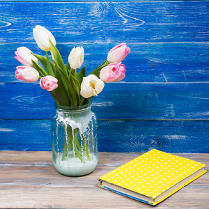 色彩艳丽的郁金香花和蓝色的木桌上的黄色书表背景。复制空间