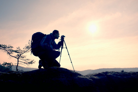 业余摄影师带镜相机的岩峰上的照片。梦幻般顽固景观 春橙色粉红色雾日出