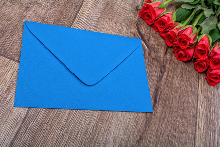 蓝色信封和木制的背景上的玫瑰