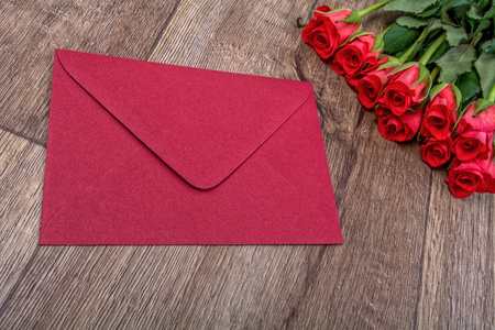 红色的信封和木制的背景上的玫瑰