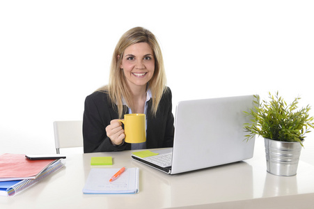 愉快的金发商业女人与咖啡杯计算机笔记本电脑上工作