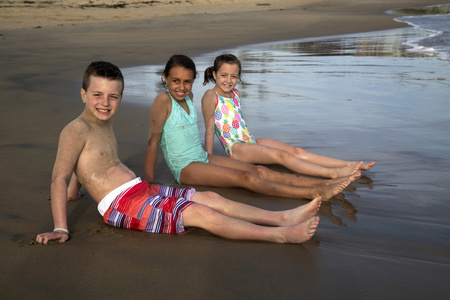 三个青春期的孩子在水微笑着在沙滩上坐