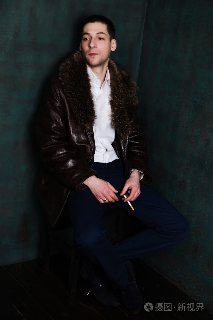 英俊的男人,穿着毛皮大衣坐在角落里认为