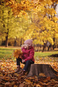 可爱微笑的女孩在散步时坐着秋叶花束