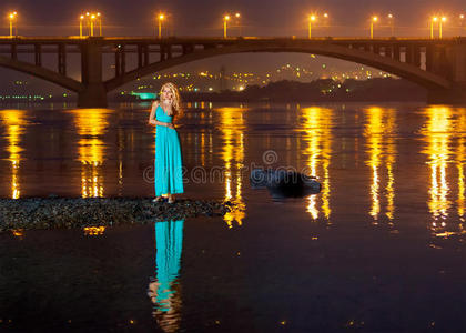 女孩晚上在河岸上的桥反射
