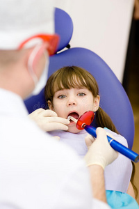 小女孩张嘴接受牙科充填干燥程序.照片