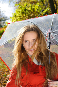 在秋天的公园里用红色的雨伞特写年轻漂亮女人的肖像