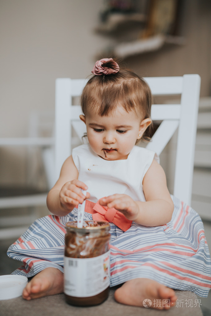 可爱的小宝贝女孩在厨房的桌子上用勺巧克力奶油吃东西和做鬼脸快乐