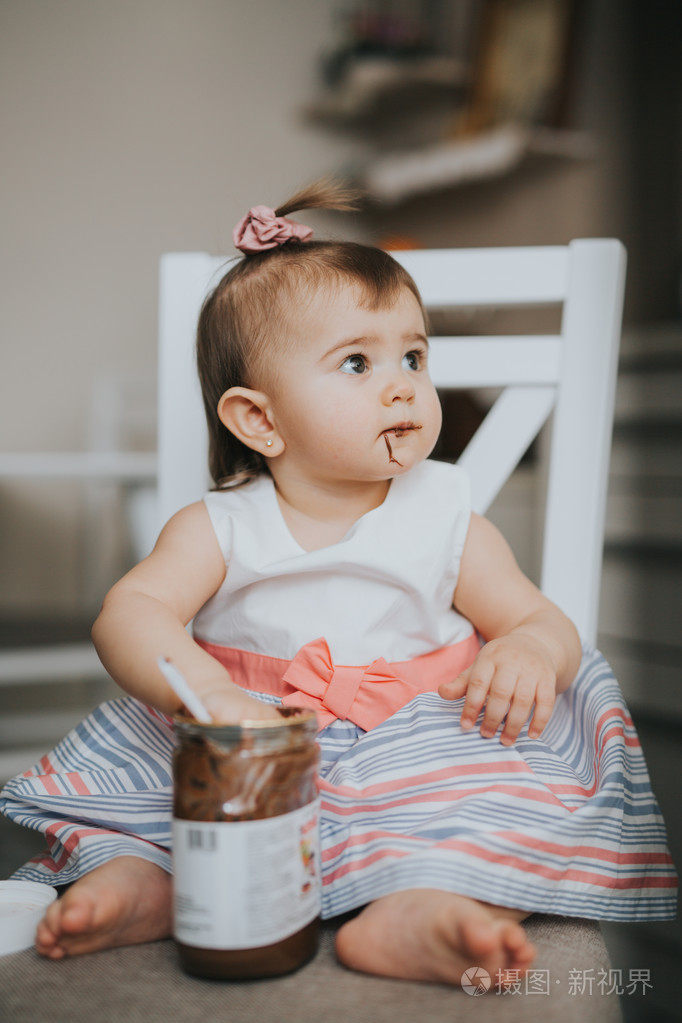 可爱的小宝贝女孩在厨房的桌子上用勺巧克力奶油吃东西和做鬼脸快乐
