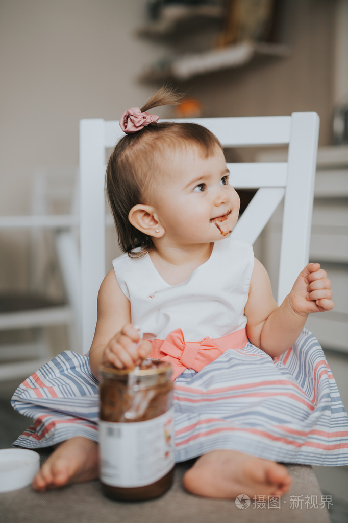 可爱的小宝贝女孩在厨房的桌子上用勺巧克力奶油吃东西和做鬼脸快乐