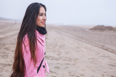 年轻漂亮的女人长的漂亮的毛的肖像穿着粉红色的外套，在秋季的北海海滩的构成