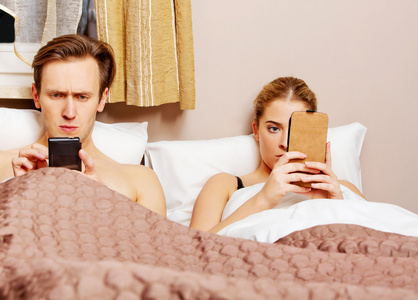 躺在床上用手机对年轻夫妇